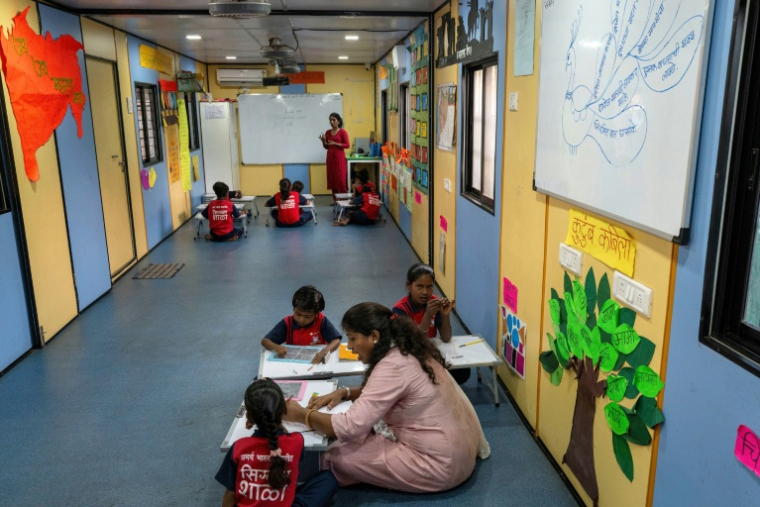 Des élèves suivent un cours à "l'école du feu rouge", qui accueille des enfants défavorisés dans des conteneurs aménagés en salles de cours sous un pont autoroutier, le 18 mai 2026 à Bombay ( AFP / Punit PARANJPE )