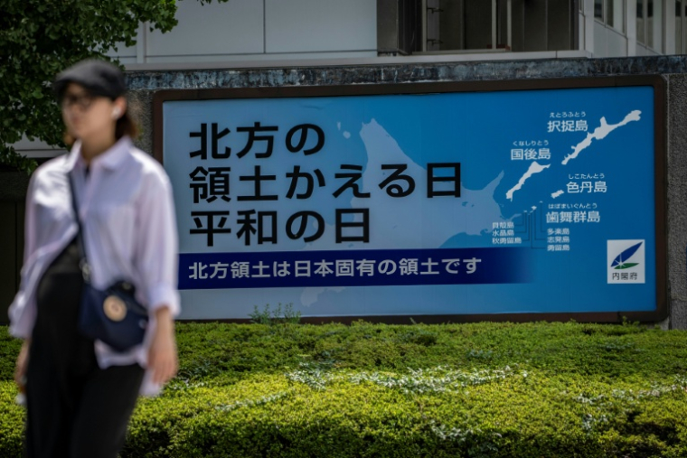 A woman walks past a Japanese government sign reading "Day of the Return of the Northern Territories, Day of Peace. The Northern Territories are an inherent part of Japan's territory,"　referring to the Russian-controlled Southern Kuril Islands claimed by Japan as its Northern Territories, in Tokyo on August 19, 2026. Bilateral relations have long been strained over the Kurils, known in Japan as the Northern Territories. After Russia's President Vladimir Putin visited the islands on August 13, Japan summoned the Russian ambassador in protest, and Russia followed suit. ( AFP / Yuichi YAMAZAKI )