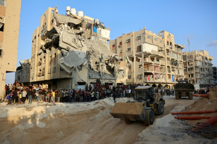 Des Palestiniens regardent une excavatrice à Khan Yunis, dans le sud de la bande de Gaza, le 17 octobre 2025 alors que le Hamas a réaffirmé son engagement à restituer toutes les dépouilles des otages sous les ruines de Gaza ( AFP / Omar AL-QATTAA )