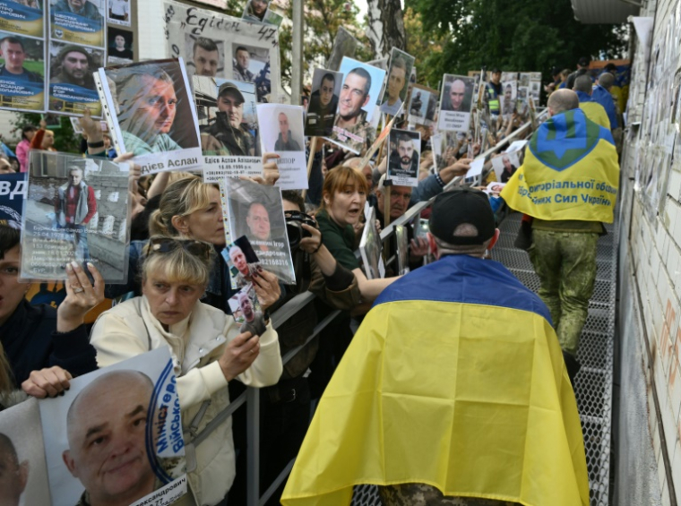 Des prisonniers de guerre ukrainiens libérés enveloppés dans le drapeau national passent devant une foule tenant des portraits de leurs proches et amis disparus ou capturés, à leur arrivée après un échange de prisonniers dans la région de Tcherniguiv, le 26 juin 2025, en Ukraine ( AFP / Genya SAVILOV )