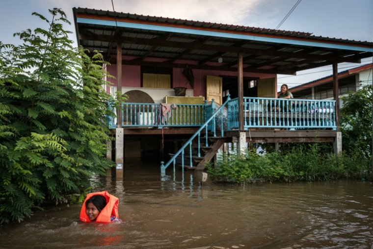 Une enfant équipée d'un gilet de sauvetage nage devant une maison inondée dans la province d'Ayutthaya, le 7 octobre 2026 en Thaïlande ( AFP / Chanakarn LAOSARAKHAM )