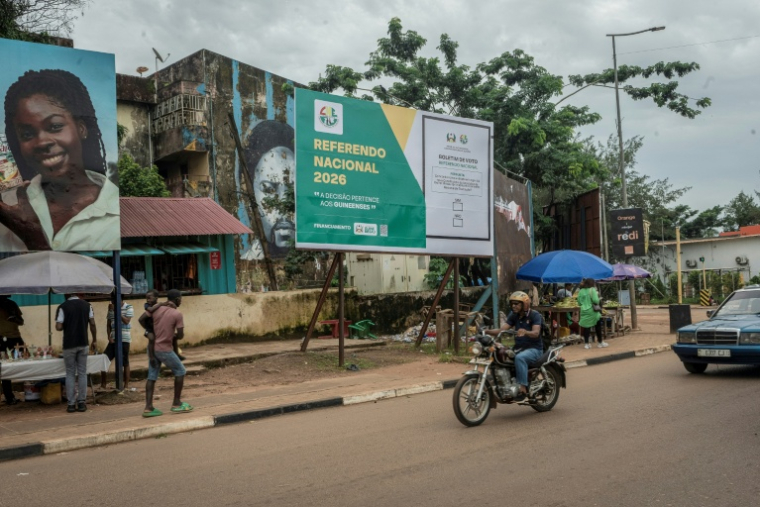 Des habitants passent le 20 août 2026 devant une affiche électorale appelant à voter lors d'un référendum constitutionnel en Guinée-Bissau. Ce référendum, organisé le 30 août par la junte au pouvoir, propose de passer à un régime présidentiel fort pour remplacer l'actuel système semi-parlementaire ( AFP / Samba BALDE )