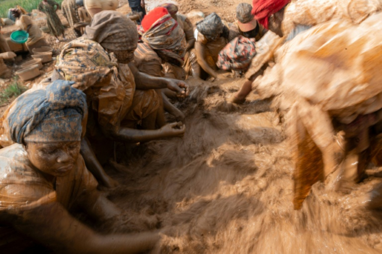 Des femmes portant des sacs en plastique par-dessus leurs vêtements  pour se protéger de la boue lavent des roches dans l’eau à la recherche de particules d’or sur un site minier artisanal à Mongbwalu, dans la province de l’Ituri, en RDCongo, le 16 juin 2026. ( AFP / Jospin Mwisha )