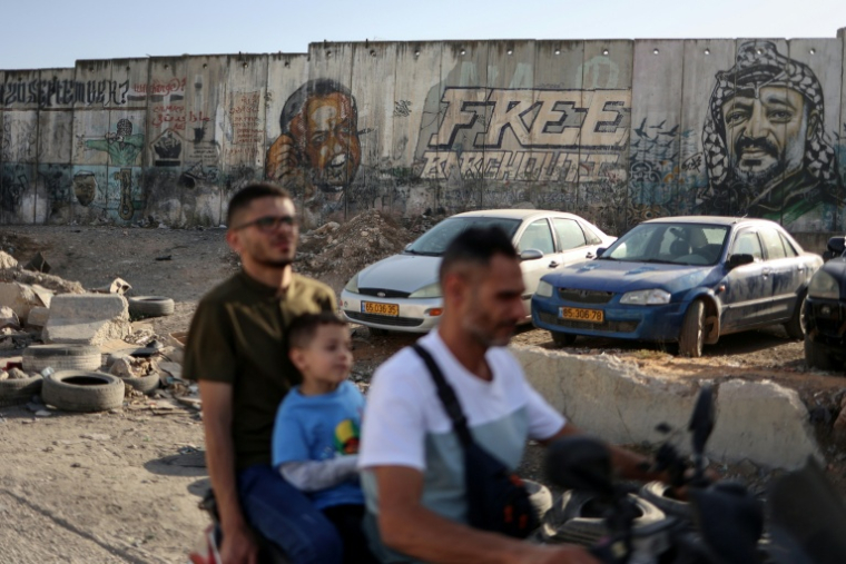 Des personnes circulent en moto devant des portraits de Marwan Barghouti (gauche) et du défunt Yasser Arafat (droite) au point de passage de Qalandiya, entre Jérusalem et Ramallah, le 22 septembre 2025.  ( AFP / Zain JAAFAR )