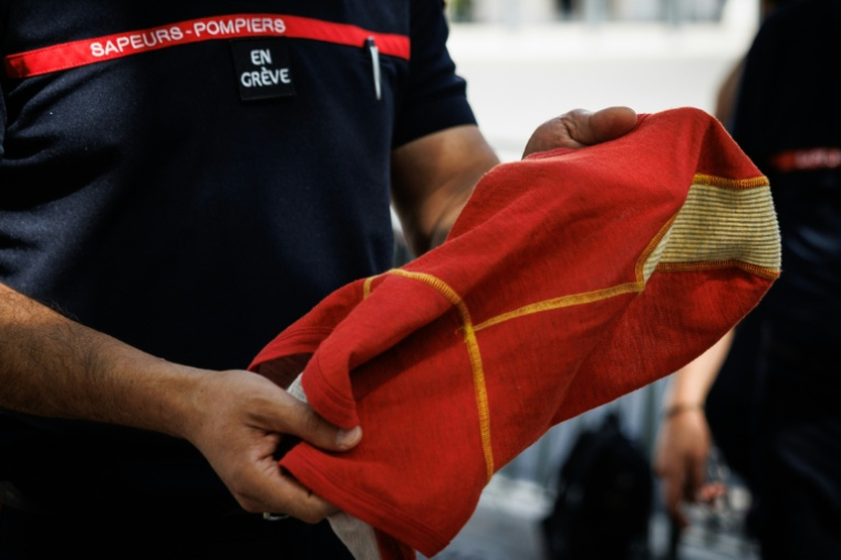 Un pompier avec "en grève" scratché sur la poitrine, devant  l'hôtel de Beauvau présente une cagoule anti-feu à Paris, le 13 août 2026 ( AFP / SIMON WOHLFAHRT )
