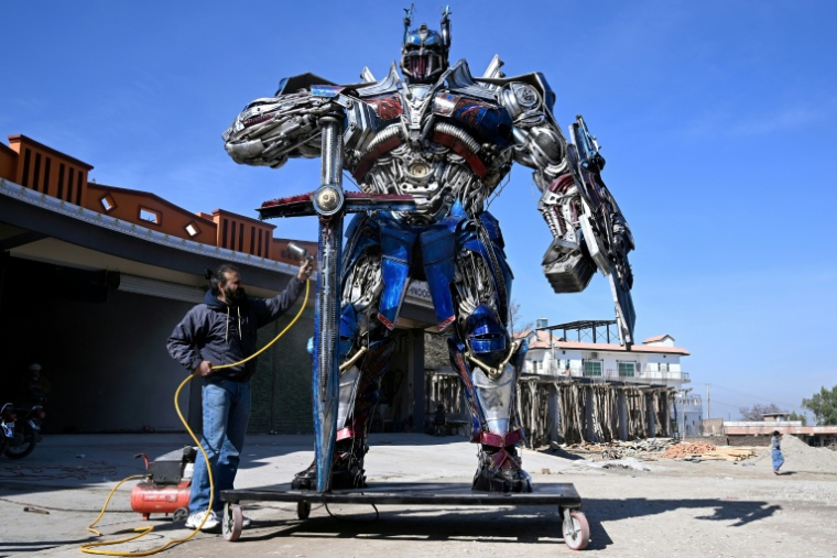 Le sculpteur Ehtisham Jadoon à côté de son Optimus Prime, personnage du film Transformers, fabriqué à partir de ferraille devant son atelier situé à la périphérie d'Islamabad, le 12 février 2026 au Pakistan ( AFP / Farooq NAEEM )