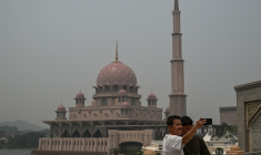 Deux personnes se prennent en photo devant une mosquée dans un air saturé par des fumées toxiques, à Putrajaya, en Malaisie, le 17 octobre 2026 ( AFP / Jam STA ROSA )