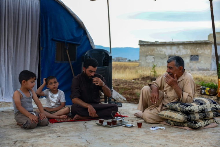 Aref Chamtan (d) prend le thé, assis devant la tente qu'il a installée près des décombres de sa maison, le 22 mai 2025 à al-Hawach, en Syrie ( AFP / Omar HAJ KADOUR )