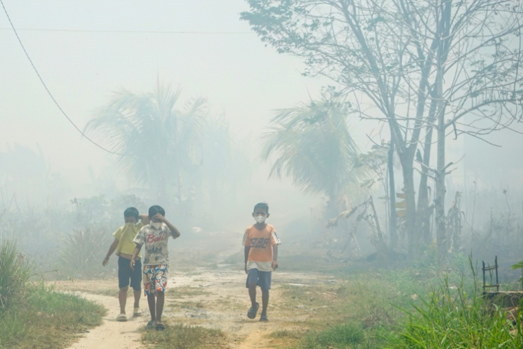 Des enfants portent des masques de protection le long d’un chemin de terre envahi par la fumée des incendies, à Banjarbaru, dans la province du Kalimantan du Sud, le 21 octobre 2026 en Indonésie ( AFP / MUDA SAGALA )