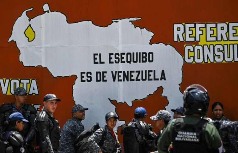 Des membres de la Police nationale bolivarienne et de la Garde nationale se tiennent à côté d'une fresque représentant une carte du Venezuela sur laquelle on peut lire "L'Essequibo appartient au Venezuela" lors d'une manifestation de la fête du Travail à Caracas le 1er mai 2025 ( AFP / Juan BARRETO )