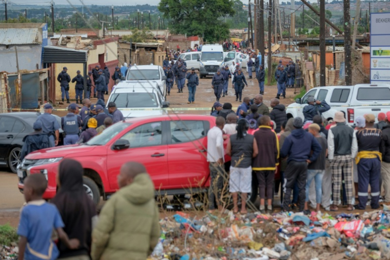 Des habitants observent des policiers rassemblés près des lieux d'une fusillade mortelle dans un bar clandestin de Bekkersdal (Afrique du Sud), le 21 décembre 2025 ( AFP / EMMANUEL CROSET                                                                                                                                                                                                                                                 )