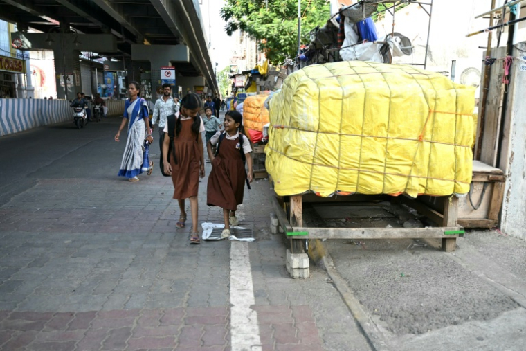 Des écolières passent le long d'un trottoir bloqué par des marchandises entreposées dans une rue à Chennai, le 9 juillet 2026 en Inde ( AFP / R.Satish BABU )