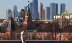 Une femme marche le long d'un pont, avec le centre d'affaires Moscow City et le mur du Kremlin visibles en arrière-plan, par une journée ensoleillée à Moscou