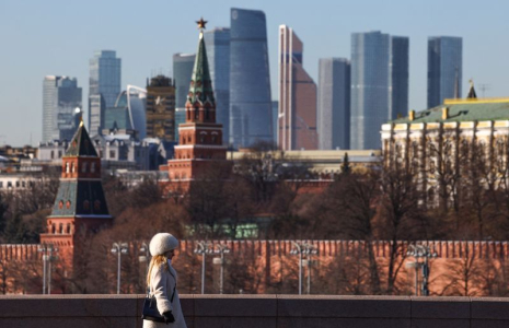 Une femme marche le long d'un pont, avec le centre d'affaires Moscow City et le mur du Kremlin visibles en arrière-plan, par une journée ensoleillée à Moscou