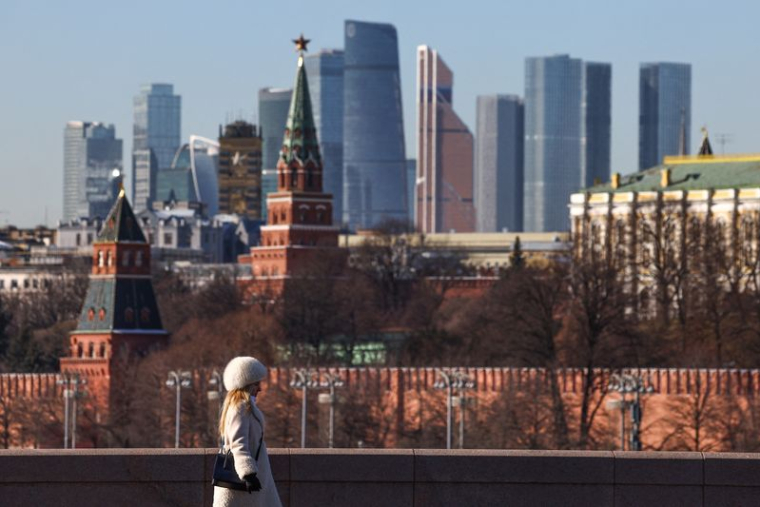 Une femme marche le long d'un pont, avec le centre d'affaires Moscow City et le mur du Kremlin visibles en arrière-plan, par une journée ensoleillée à Moscou