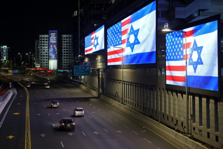 Des voitures passent le 4 mars 2026 devant des écrans géants installés le long de l'autoroute à Tel Aviv, affichant les drapeaux des Etats-Unis et d'Israël ( AFP / Jack GUEZ )