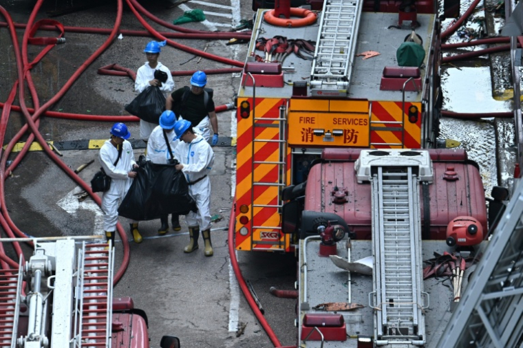 Des policiers de l’unité d’identification des victimes de catastrophes, vêtus de combinaisons intégrales de protection blanches, transportent des sacs devant le complexe résidentiel de Wang Fuk Court à Hong Kong  la suite de l’incendie meurtrier survenu trois jours auparavant ( AFP / Philip FONG )