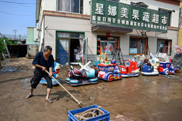 Un homme âgé déblaye la boue devant un marché inondé après de fortes pluies dans le village de Taishitun, dans le district de Miyun, à la périphérie de Pékin, le 28 juillet 2025 ( AFP / Jade GAO )