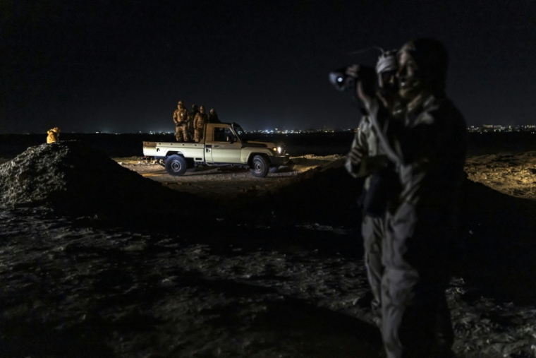 Des garde-côtes mauritaniens  utilisent des jumelles de vision nocturne pour surveiller les activités le long du littoral, tandis que d'autres se tiennent à l'arrière d'une camionnette à Nouadhibou (Mauritanie), le 23 avril 2026 ( AFP / PATRICK MEINHARDT )