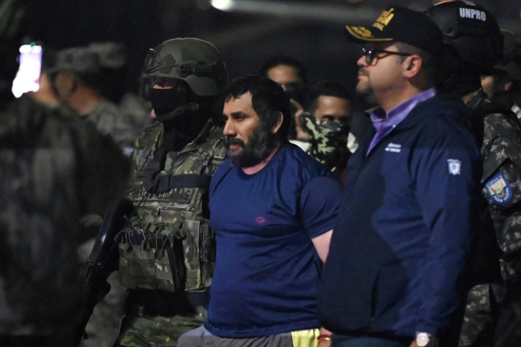 Le trafiquant de drogue Adolfo Macias (c), alias Fito, gardé par le ministre de l'Intérieur équatorien John Reimberg (2e d) et du personnel militaire à son arrivée à la base aérienne de Guayaquil, après sa recapture, le 25 juin 2025 à Manta, dans la province de Manabi, en Équateur ( AFP / Marcos PIN )
