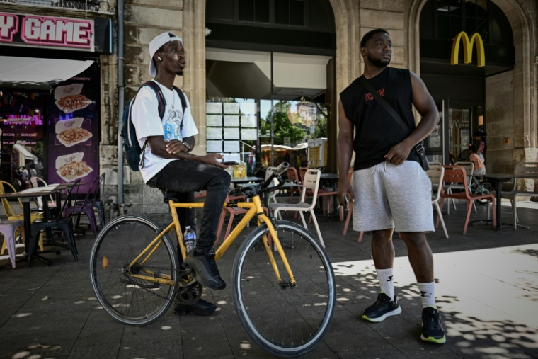 Deux livreurs à vélo se reposent pendant une vague de chaleur estivale près des restaurants en attendant des commandes, à Bordeaux, le 7 juillet 2026 ( AFP / Philippe LOPEZ )