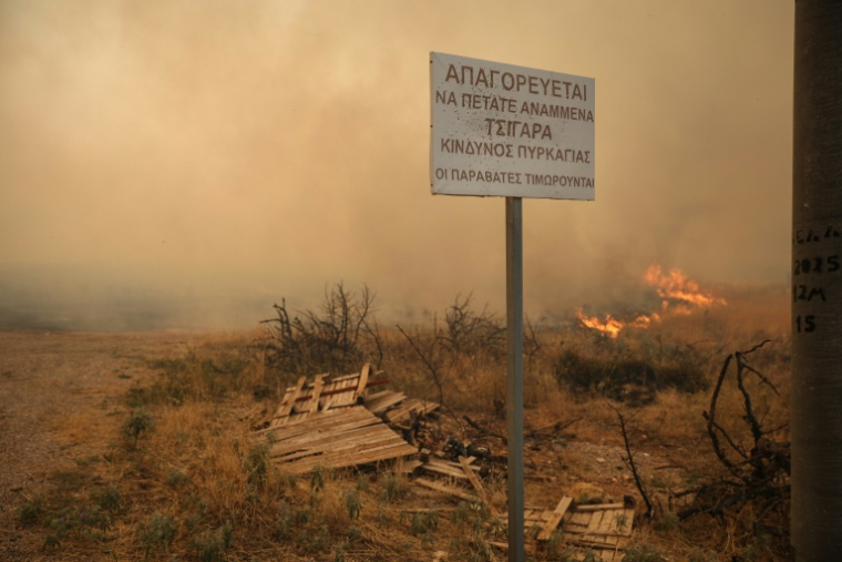 "Il est interdit de jeter des cigarettes, cela peut provoquer un incendie", dit un panneau dans la région de Megara en proie à un feu, le 3 août 2026. ( AFP / Aris Oikonomou )