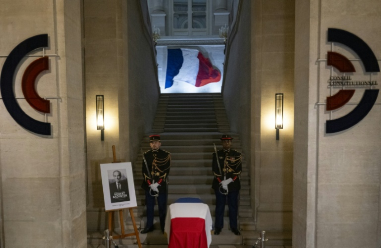 Des gardes républicains montent la garde près du portrait de feu Robert Badinter et d'un cercueil recouvert d'un drapeau français lors d'une veillée funèbre au Conseil constitutionnel à Paris, le 8 octobre 2025 ( AFP / Martin LELIEVRE )