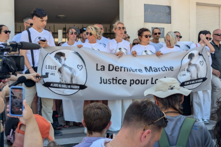 La mère de Louis (C), un adolescent de 17 ans battu à mort fin juin dans un guet-apens, se tient derrière une banderole lors d'une nouvelle marche en mémoire de son fils, le 5 juillet 2026 à Narbonne ( AFP / Valentin GRAFF )