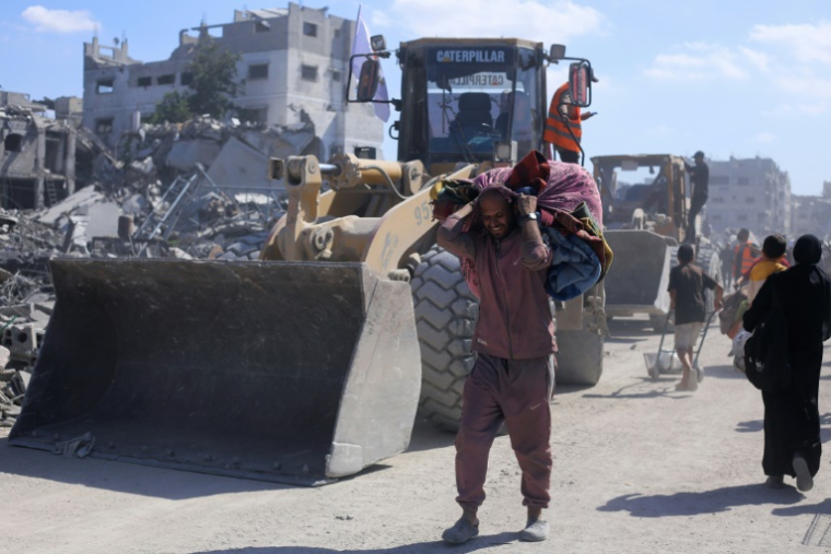 Des déplacés palestiniens passent près de bulldozers de la municipalité de Gaza chargés de déblayer les décombres des bâtiments situés sur les axes principaux et dans les rues de la ville de Gaza, le 14 octobre 2025 ( AFP / - )