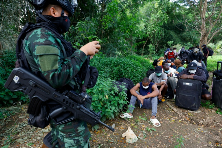 Un soldat monte la garde devant des personnes de différents pays, qui travaillaient au complexe du parc KK en Birmanie et ont traversé la rivière Moei pour se rendre en Thaïlande, dans le district de Mae Sot, dans la province de Tak, le 24 octobre 2025 ( THAI NEWS PIX / Sarot Meksophawannakul )