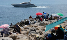 Un bateau de luxe passe devant un groupe de migrants installés sur les rochers de la digue à la frontière de Saint Ludovic, en Méditerranée, entre Vintimille et Menton