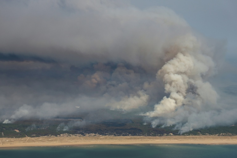 Plan aérien d'un incendie de forêt au nord du bassin d'Arcachon, dans le sud-ouest de la France, le 24 juillet 2026This aerial photograph shows smoke emanating from the wildfire north of the Arcachon basin (seen Top) covering the forest, with a view of a beach and the Atlantic Ocean (bottom) near Lege-Cap-Ferret, southwestern France, on July 24, 2026.  France has been battered by three heatwaves since May as part of increasingly common extreme weather episodes linked to climate change, causing excess deaths, drying up rivers and fuelling wildfires. Scientists have long warned that climate change caused by human use of fossil fuels will make periods of drought more intense and longer-lasting, creating the ideal conditions for wildfires. ( AFP / ROMAIN PERROCHEAU )