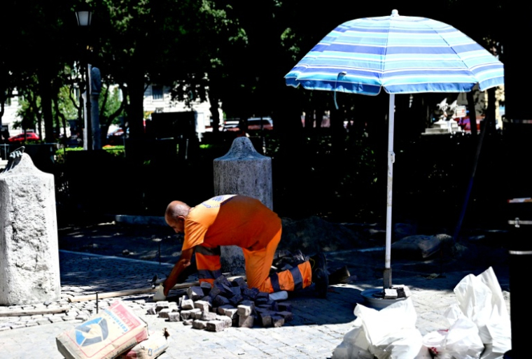 Un ouvrier pose des pavés à l'ombre d'un parasol sur la Piazza Mazzini, par une chaude journée d'été à Rome, le 1er juillet 2025. ( AFP / Tiziana FABI )
