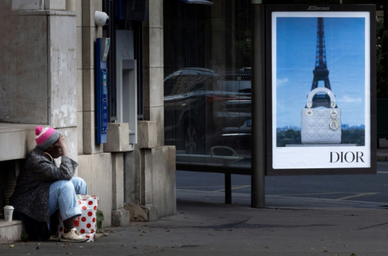 Une personne sans abri à Paris, devant une publicité pour une marque de luxe, le 8 juillet 2025 ( AFP / JOEL SAGET )