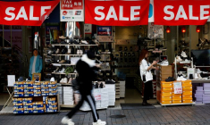 Un passant passe devant un magasin de détail affichant des bannières "SALE" à Tokyo