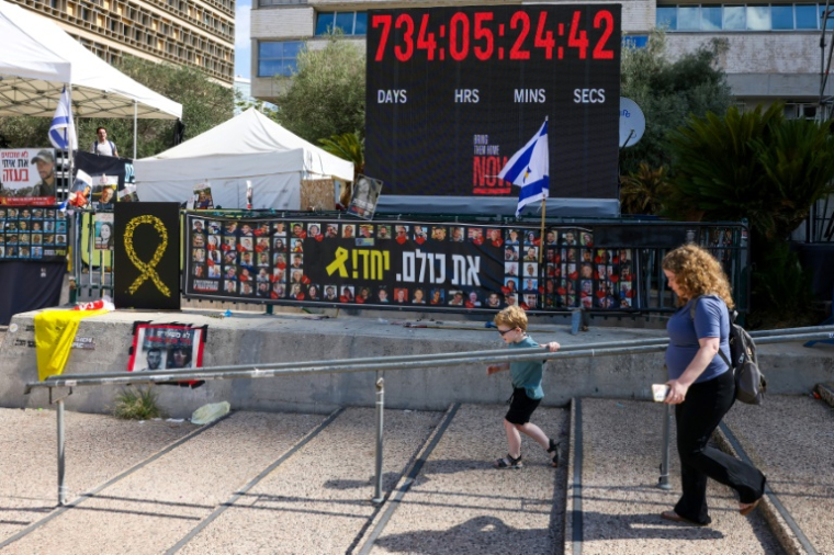 Une femme et un enfant passent devant des photos d'otages retenus à Gaza, sur la "place des Otages" à Tel-Aviv, le 10 octobre 2025 ( AFP / AHMAD GHARABLI )
