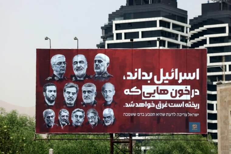 Les portraits de hauts gradés tués dans les attaques israéliennes sont affichés dans une rue de Téhéran, avec le slogan en farsi: "Israël doit savoir qu'il se noiera dans le sang qu'il a fait couler", le 26 juin 2025 ( AFP / ATTA KENARE )