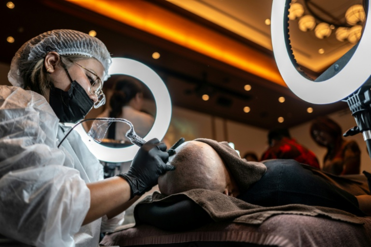 Un tatoueur spécialisé dans le tatouage du cuir chevelu lors d'un concours à Naha, dans la préfecture d'Okinawa, au Japon, le 8 juillet 2026 ( AFP / Philip FONG )
