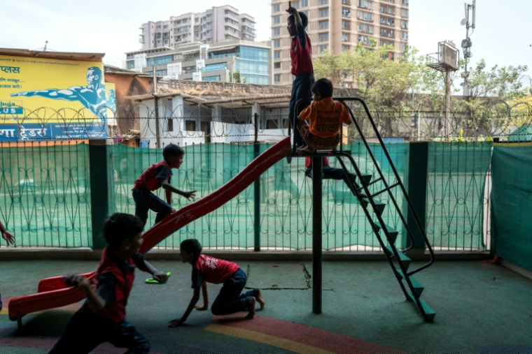 Des élèves jouent dans  "l'école du feu rouge", qui accueille des enfants défavorisés dans des conteneurs aménagés en salles de cours sous un pont autoroutier, le 18 mai 2026 à Bombay ( AFP / Punit PARANJPE )