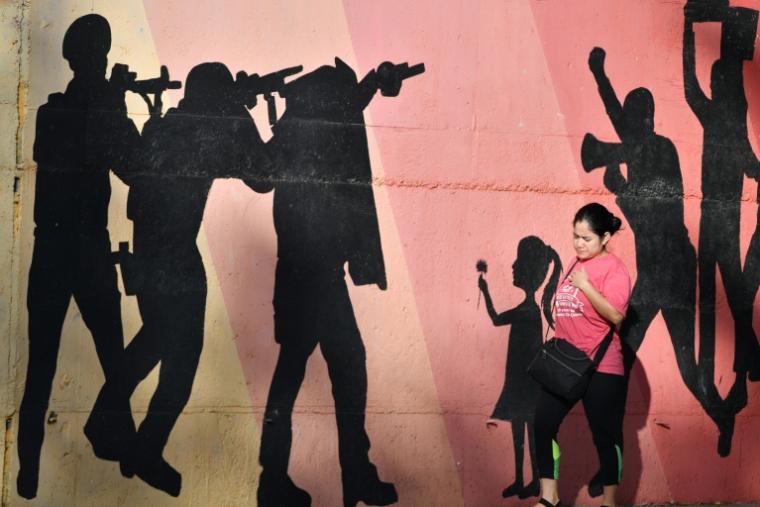 Une femme passe devant une fresque murale représentant des hommes armés visant des manifestants, allusion à la répression policière, dans une avenue de Tegucigalpa, le 27 novembre 2025 ( AFP / Orlando SIERRA )
