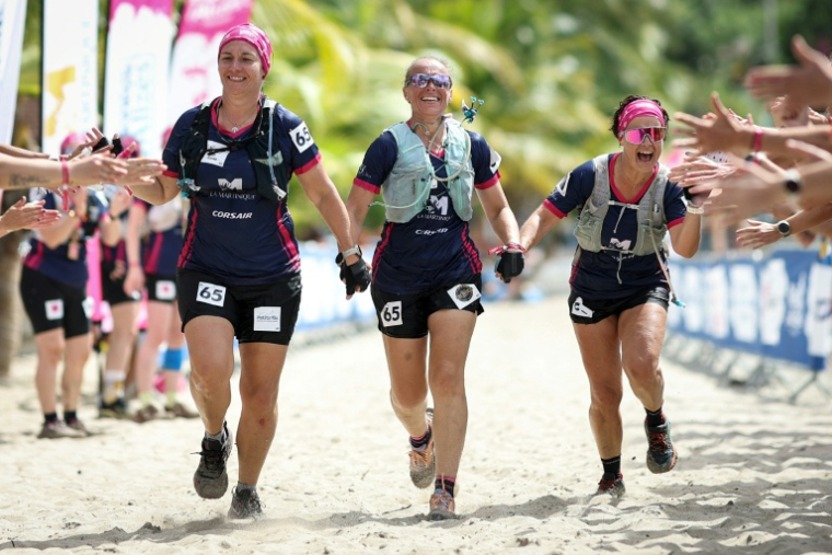 Sonia Latapie (c), souffrant d'insuffisance rénale et atteinte d'un cancer du sein, membre de l'équipe "Les Reines du cœur", tient la main de ses coéquipières Carole Loussalez (d) et Alexia Elineau (g), alors qu'elles franchissent la ligne d'arrivée du "Raid des Alizés", aux Anses-d'Arlet, le 29 novembre 2025 en Martinique ( AFP / Anne-Christine POUJOULAT )