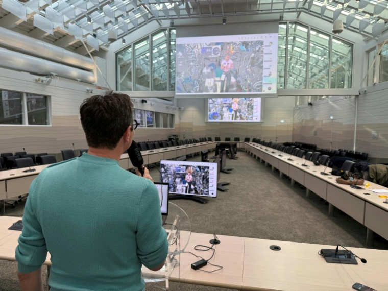 Le journaliste de l'AFP Frédéric Bourigault (à gauche) interroge l'astronaute de l'ESA Sophie Adenot (sur les écrans) qui se trouve à bord de la Station spatiale internationale (ISS), au siège de l'Agence spatiale européenne (ESA) à Paris, le 26 février 2026 ( AFP / Jacques-Alexandre BRUN )
