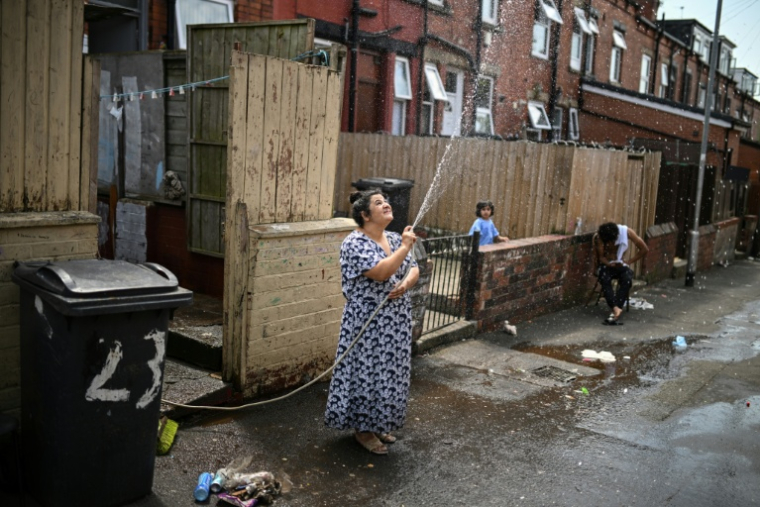 Une femme asperge une allée devant chez elle pour rafraichir à Leeds en Angleterre le 25 juin 2026 ( AFP / Oli SCARFF )
