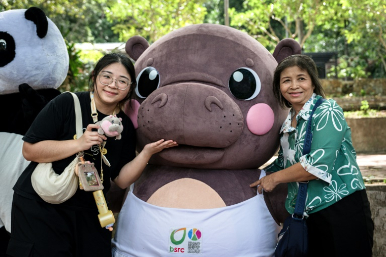 Des visiteuses posent avec une mascotte du bébé hippopotame pygmée Moo Deng au zoo de Khao Kheow à Chonburi, le 10 juillet 2025 en Thaïlande ( AFP / Chanakarn Laosarakham )