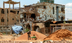 Un ouvrier pellette des cailloux dans une brouette près d'un bâtiment fortement endommagé de la banlieue de Lambab, à la périphérie de Khartoum, le 30 juillet 2025 au Soudan ( AFP / Ebrahim Hamid )