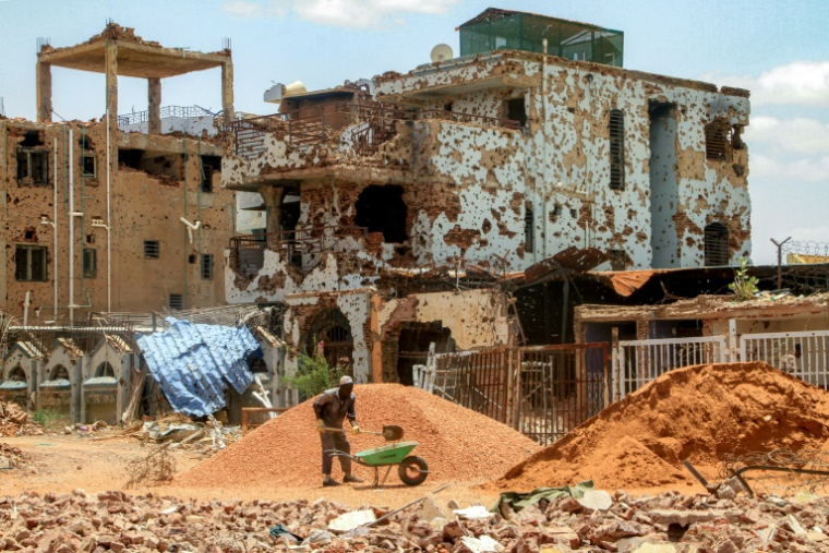 Un ouvrier pellette des cailloux dans une brouette près d'un bâtiment fortement endommagé de la banlieue de Lambab, à la périphérie de Khartoum, le 30 juillet 2025 au Soudan ( AFP / Ebrahim Hamid )