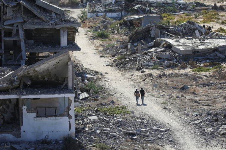 Des Palestiniens marchent près de bâtiments détruits, le 14 octobre 2025 dans la zone d'al-Zahra dans la bande de Gaza ( AFP / Eyad BABA )