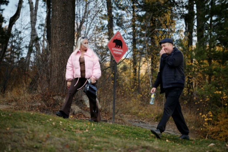 Des promeneurs passent devant un panneau avertissant de la présence d'ours sur un sentier de randonnée dans le parc national du lac Baïkal, dans la région d'Irkoutsk, le 9 octobre 2026 en Sibérie ( AFP / TATYANA MAKEYEVA )
