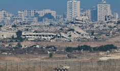 Un véhicule blindé de transport de troupes manœuvre le long du côté israélien de la frontière, tandis que la destruction à Gaza est visible
