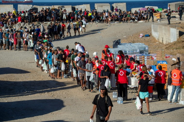 Des bénévoles de la Croix-Rouge distribuent de la nourriture aux migrants restés à Ceuta, sur une plage de l'enclave espagnole au Maroc, le 22 août 2026 ( AFP / Antonio Sempere )